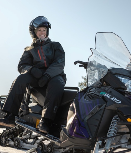 A woman sitting sideways on an electric snowmobile and laughing.