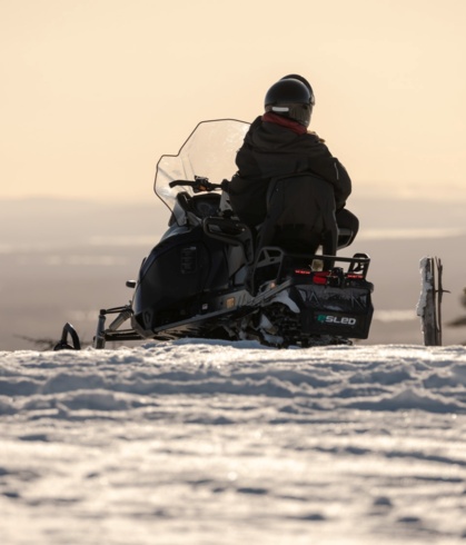 A person on a snow scooter on top of a hill under a sunset.