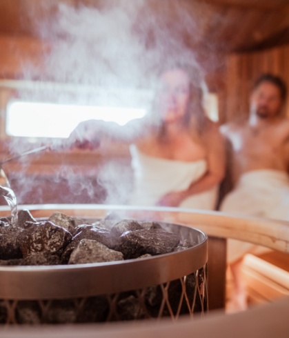 A couple in the steam sauna, with the woman pouring water on the coals.