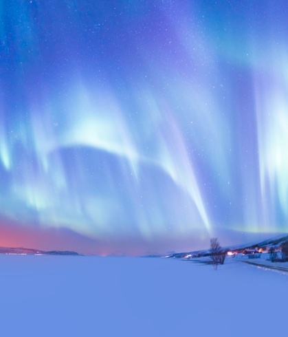 Northern lights above a frozen lake, with a small village on its right bank.