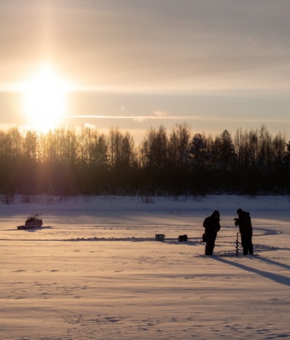 Two people ice fishing under the sunset.