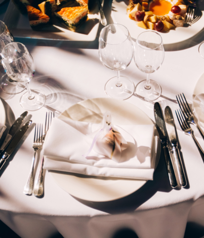 Elegantly folded napkins and cutlery on a round table dressed in white tablecloth.