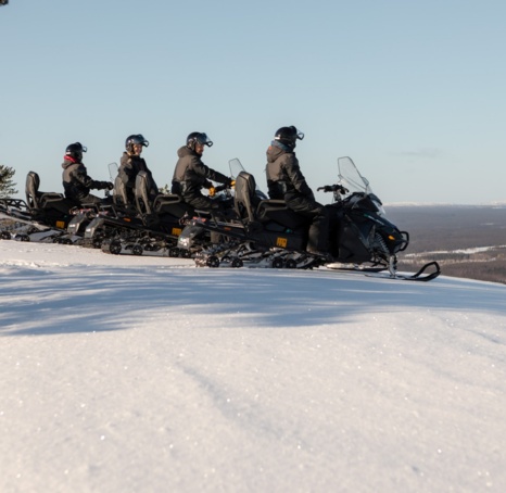 A line of people on snow electro mobiles getting ready to ride downhill.