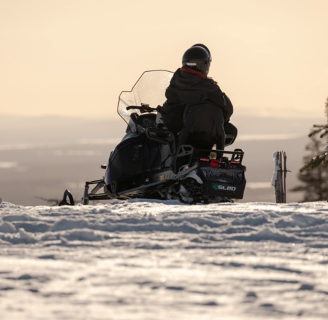 A person on a snow scooter on top of a hill under a sunset.