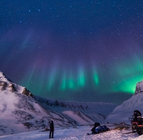 Northern lights in a valley, turning from blue, through purple to green as they descend.