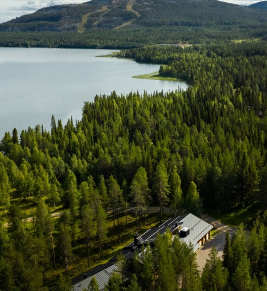 Summer Lapland a lake surrounded by bright-green trees, amongst which sits the Sunday Morning Resort