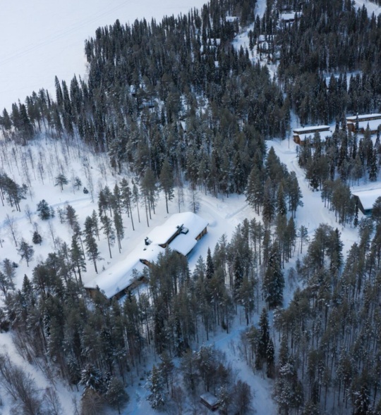 A snow-covered lodge visible from above and surrounded by trees.