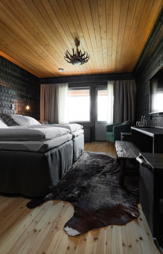 A timber lodge bedroom, with 2 single beds, a bear skin on the floor and large windows in the back.