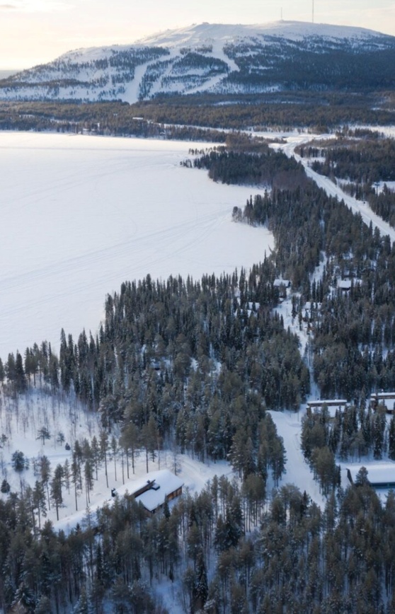 Snow-covered lake, with a lakeside resort nestled in the forest on its right bank.