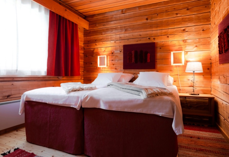 A two-person bedroom in a wooden lodge, illuminated with warm light.
