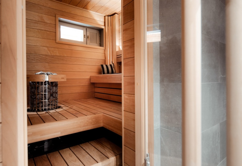 The interior of a tiny wooden sauna, with a shower on the right side and the benches in the corner.