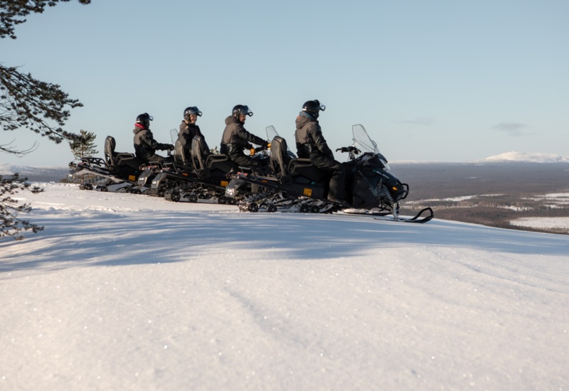 A line of people on snow electro mobiles getting ready to ride downhill.