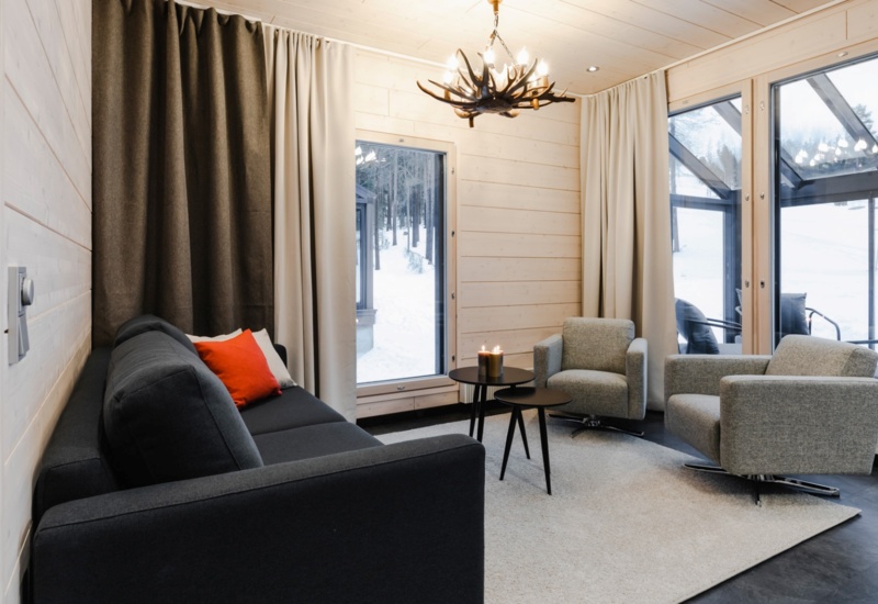 A living room with one couch, 2 sofas and a two round tables with lighted candles on them.