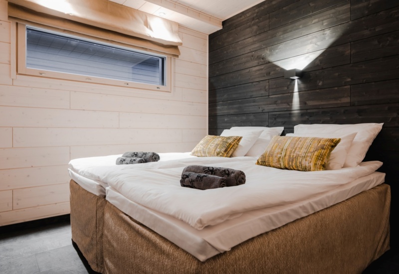 Bedroom in a wooden lodge, with white wood used on the side and black wood on the back wall.