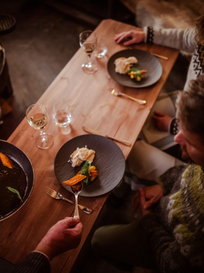 Gourmet dishes served on black, textured plates along with a glass of white wine.