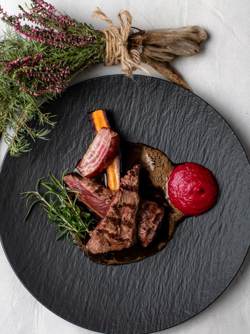 Slices of grilled meat drizzled with a rich brown jus and striped root vegetables.