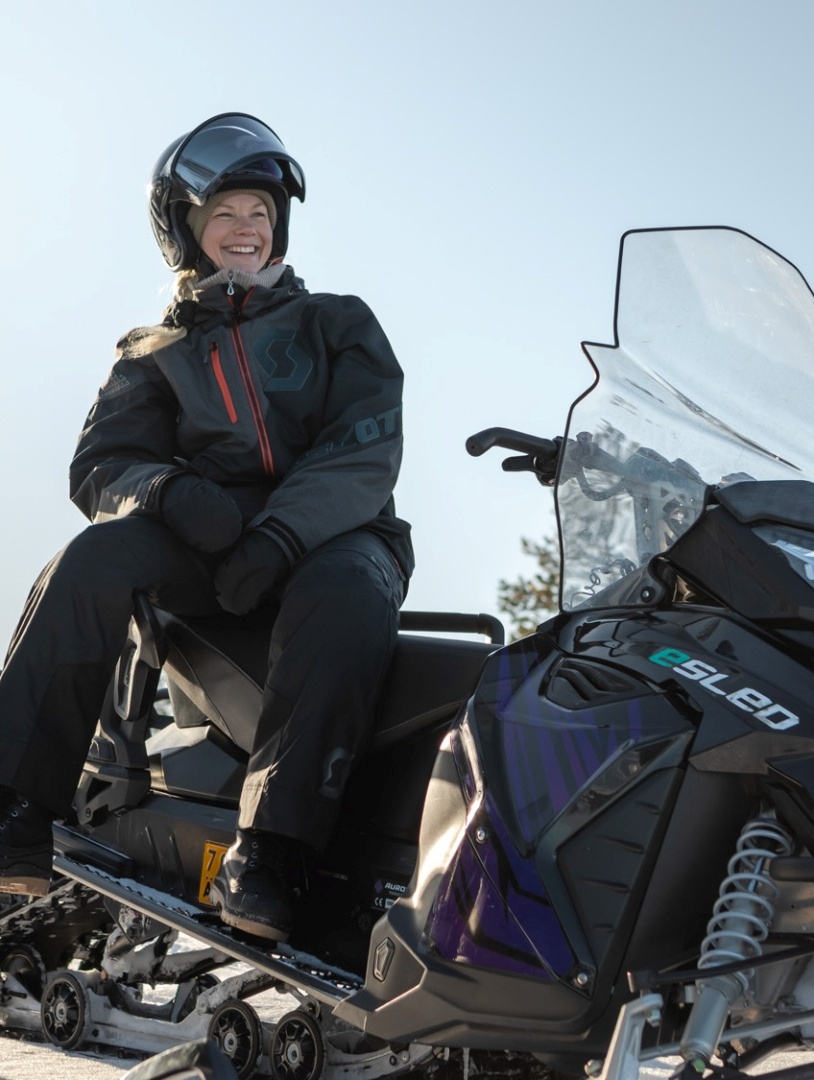 Frauen genießen winterliches Abenteuer auf Elektro-Schneemobilen vor verschneiter Waldkulisse