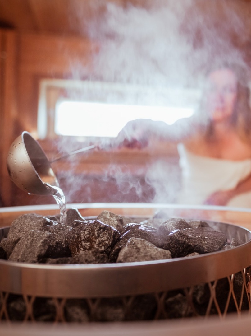 A couple in the steam sauna, with the woman pouring water on the coals.