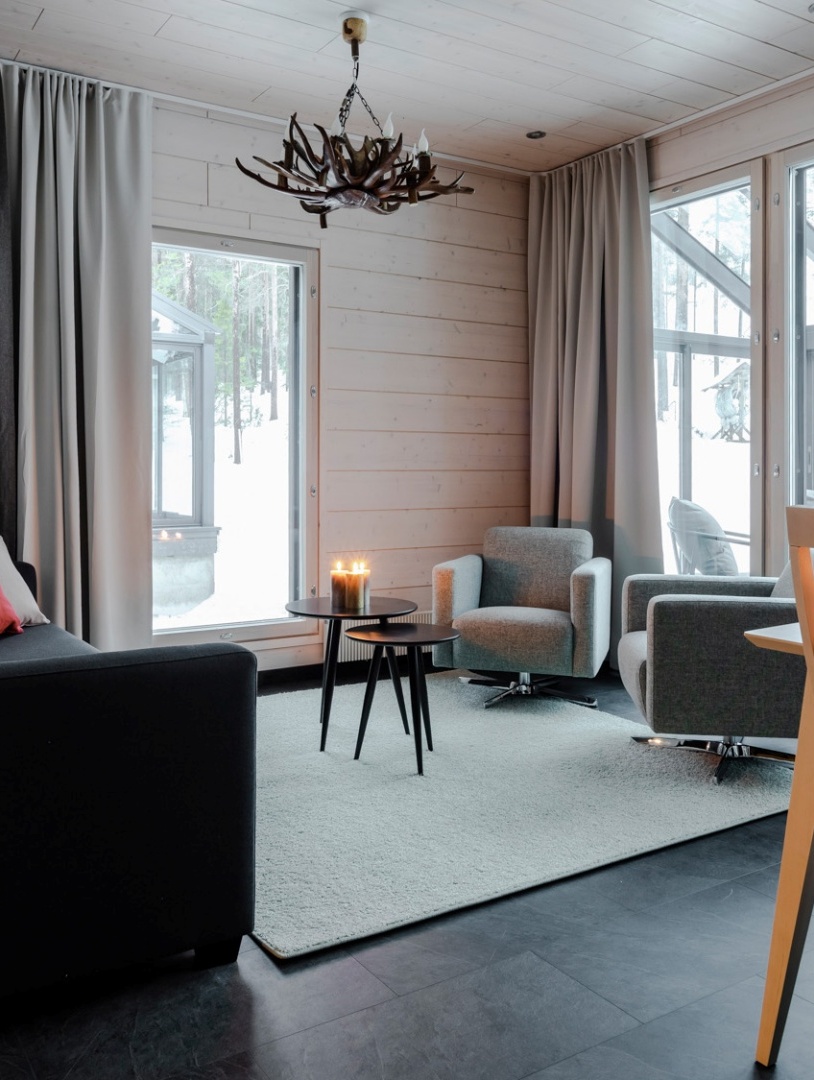 A living room with one couch, 2 sofas and a two round tables with lighted candles on them.