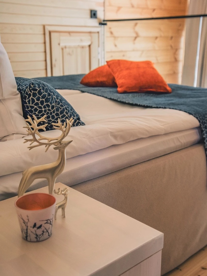 A bed for two in a wooden lodge, next to it a nightstand with a reindeer figure.