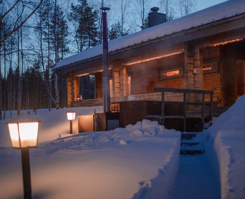 A cozy wooden lodge nestled in the snow in the evening, illuminated by warm light.
