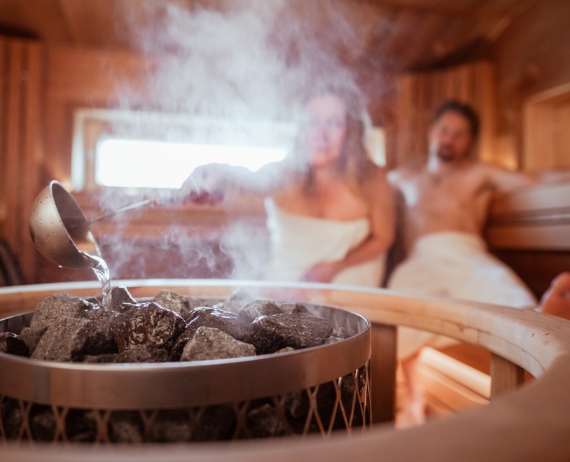 A couple in the steam sauna, with the woman pouring water on the coals.