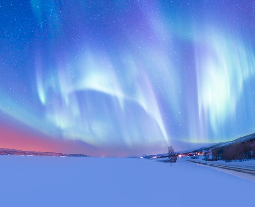 Northern lights above a frozen lake, with a small village on its right bank.