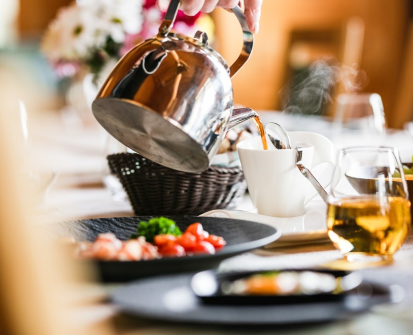 A server pours hot coffee into a white cup at a beautifully set breakfast table at Restaurant Aihki, with steam rising and fresh dishes and juices arranged around the table.
