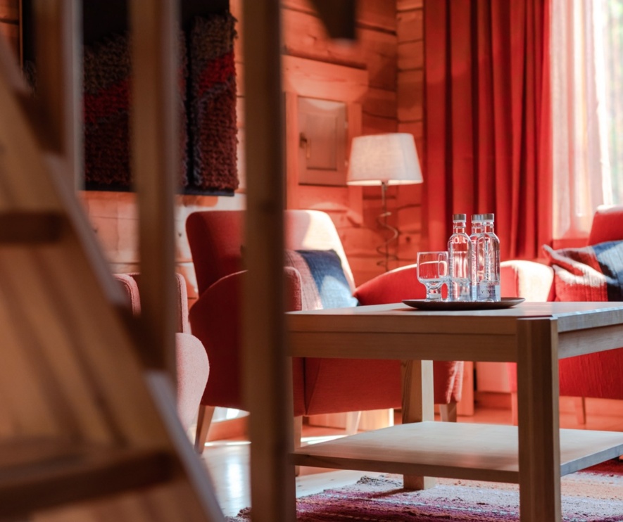 A living room with a small coffee table, red curtains in the background and a red sofa & couch.