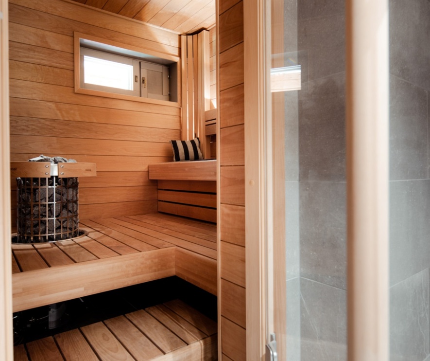 The interior of a tiny wooden sauna, with a shower on the right side and the benches in the corner.