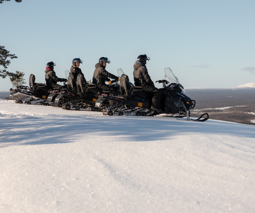 A line of people on snow electro mobiles getting ready to ride downhill.