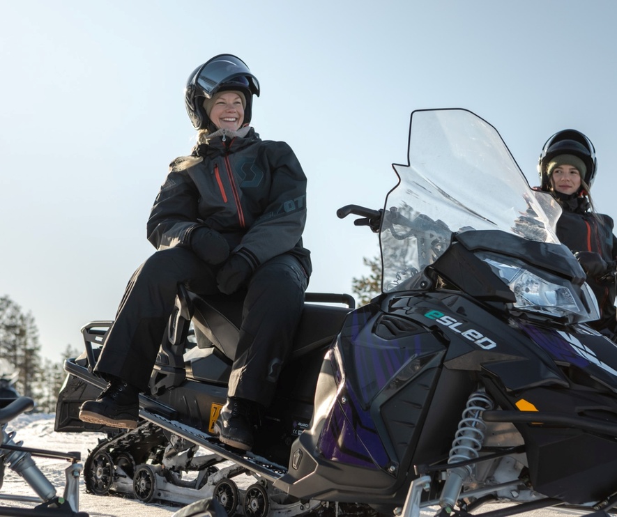 Femmes profitant d'une aventure hivernale en motoneige électrique avec forêt enneigée en arrière-plan