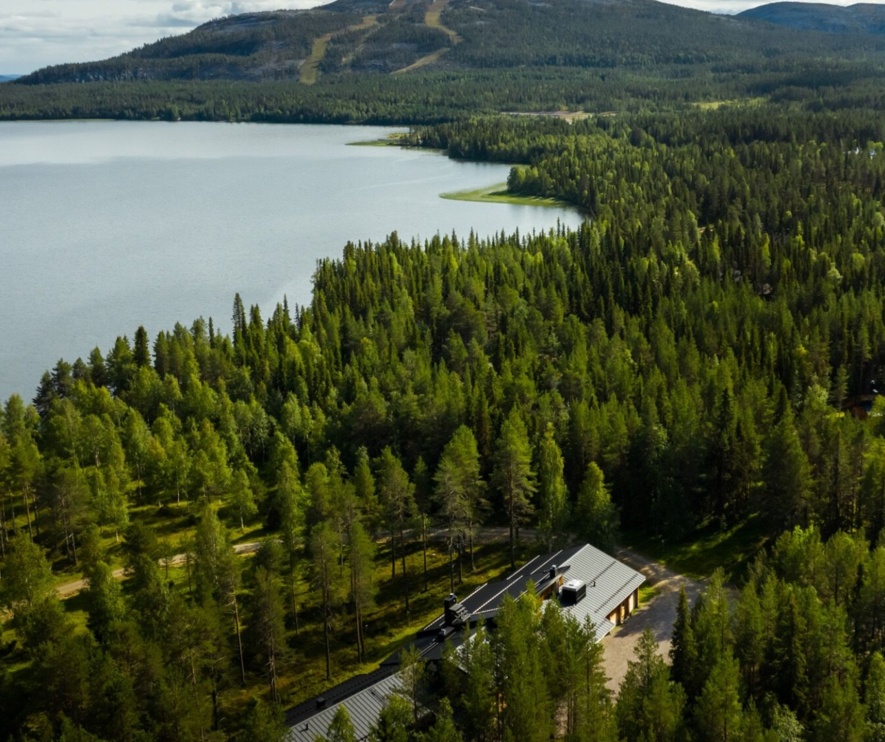 Summer Lapland a lake surrounded by bright-green trees, amongst which sits the Sunday Morning Resort