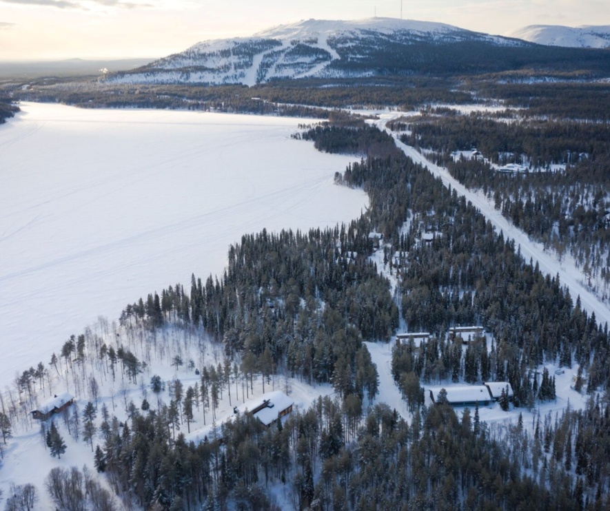 Snow-covered lake, with a lakeside resort nestled in the forest on its right bank.