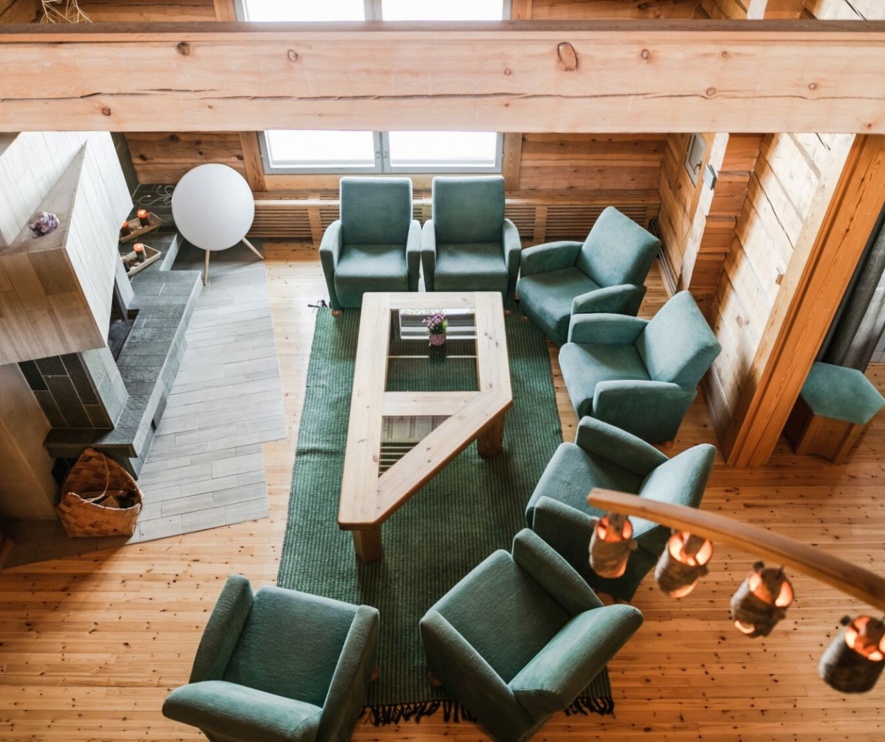 A set of sofas around a coffee table placed in front of a marble fireplace in a timber lodge.