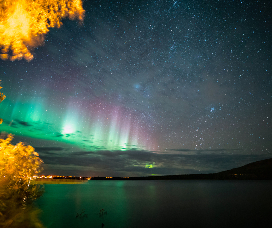Vibrant northern lights over a tranquil lake with autumn trees glowing gold under a starry night sky