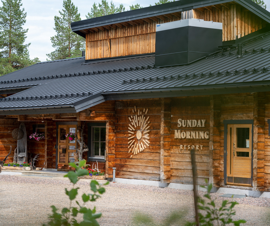 木制乡村度假屋 'Sunday Morning Resort'，黑色金属屋顶、花篮、木质入口，近处有一只驯鹿