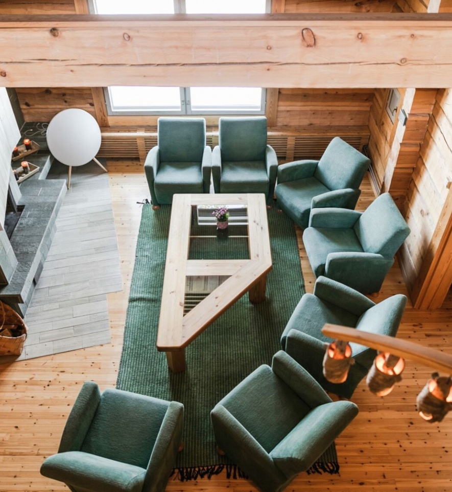 A set of sofas around a coffee table placed in front of a marble fireplace in a timber lodge.