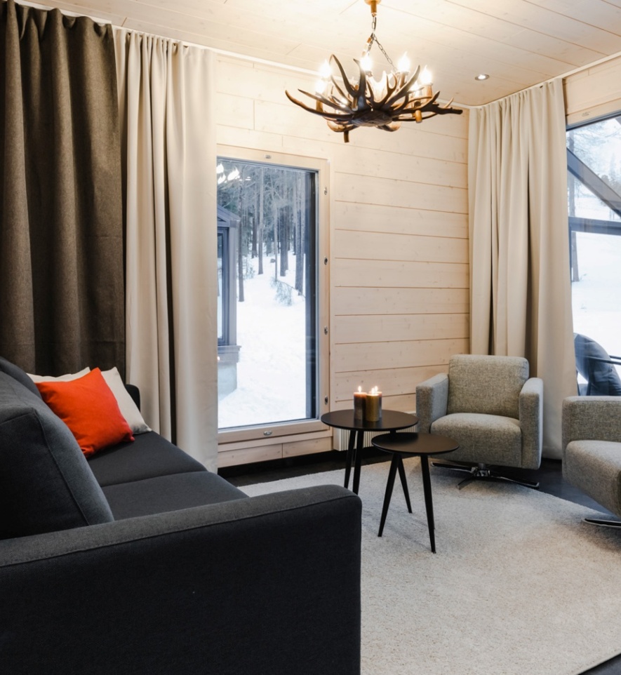 A living room with one couch, 2 sofas and a two round tables with lighted candles on them.