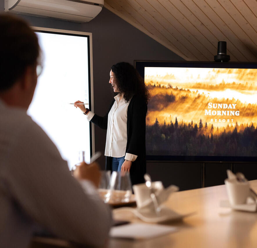 A woman in a wooden conference room, writing on an interactive whiteboard.