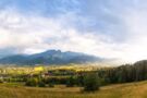 A green meadow with scattered trees set against the majestic peaks of the Tatra Mountains.