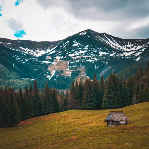 Drewniana górska chata u podnóża ośnieżonych szczytów Tatr