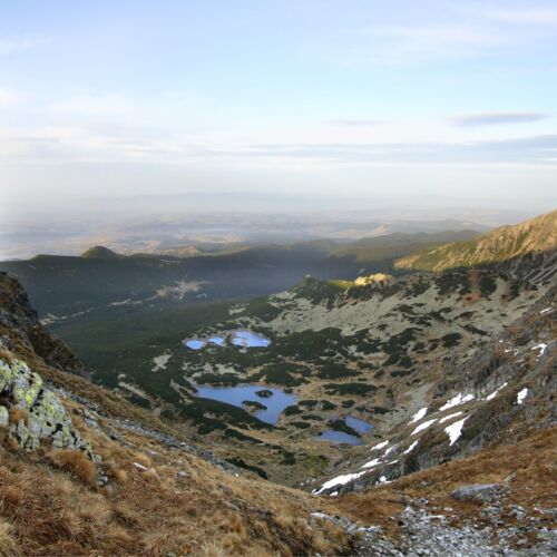 Panorama doliny widziana ze szczytu góry, z rozciągającymi się lasami i łąkami.