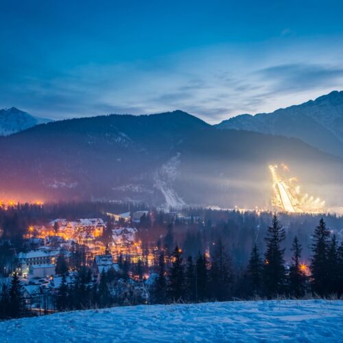 Wieczorny widok na Zakopane z gór, z migoczącymi światłami miasta tworzącymi nastrojową atmosferę.