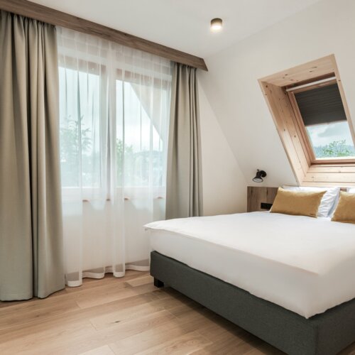 Dwuosobowe łóżko przy oknie, z którego roztacza się widok na malownicze Zakopane i okoliczne góry.