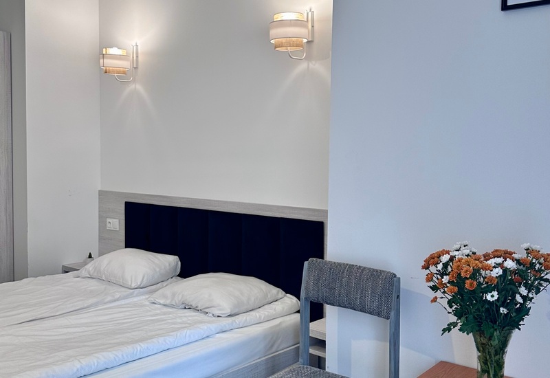 Klimatyczny pokój hotelowy z podwójnym łóżkiem, nocnymi lampkami, kwiatami i planszą do gry na drewnianym stole