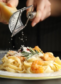 Ręce ścierają parmezan na krewetkowe fettuccine z rozmarynem, kieliszek wina w tle