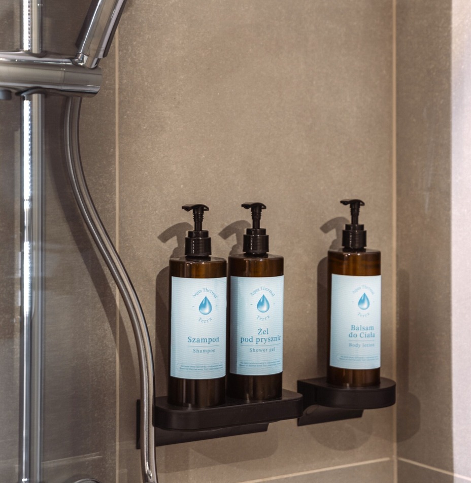 Chrom-Handbrause über drei Wandspendern mit Shampoo, Duschgel und Körperlotion an grauer, gefliester Duschwand