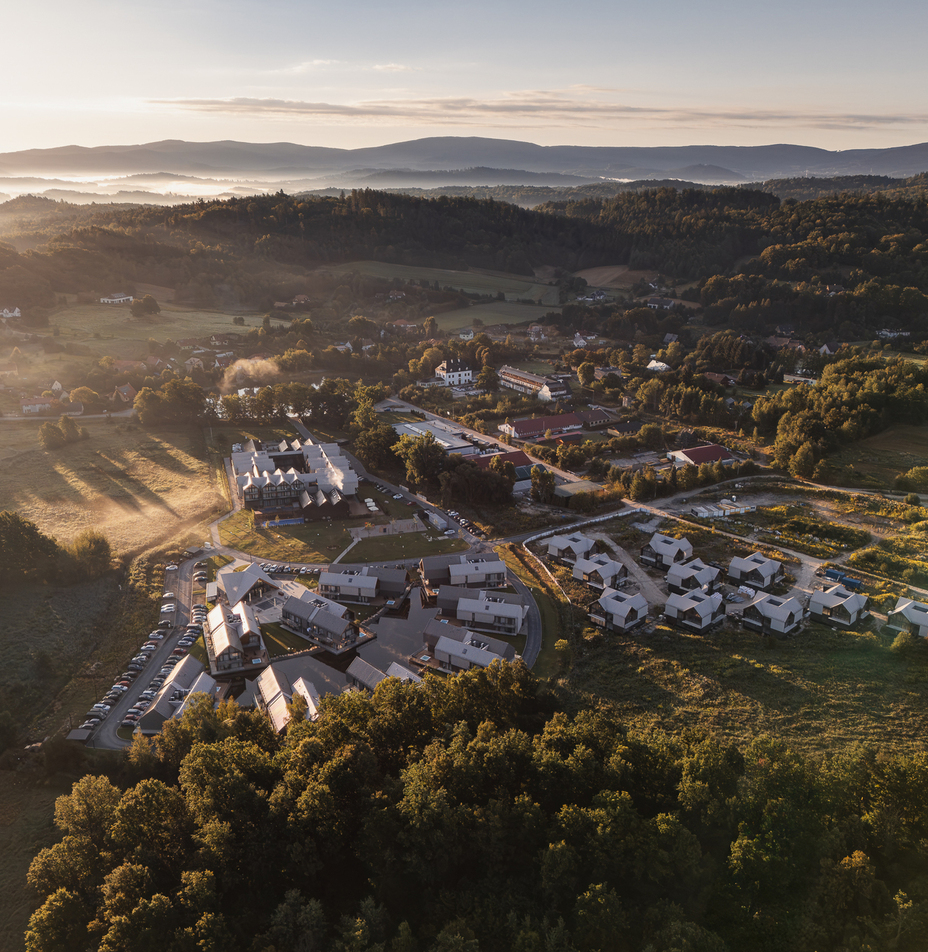 Resort mit modernen Ferienhäusern und Haupthotel im Wald, Parkplatz, nebelverhangene Hügel und Berge im Sonnenaufgang.