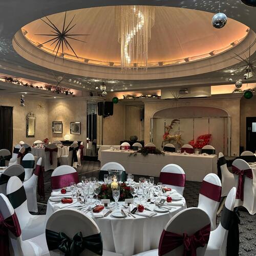 Elegant hotel ballroom with domed ceiling and chandelier; round tables set for a festive banquet with white linens and sashed chairs.
